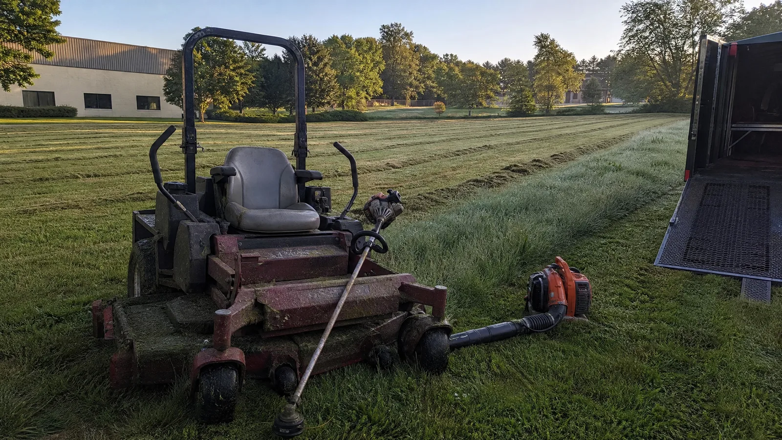 Commercial zero-turn mower parked on a freshly cut commercial lawn with a trimmer leaning against its deck
