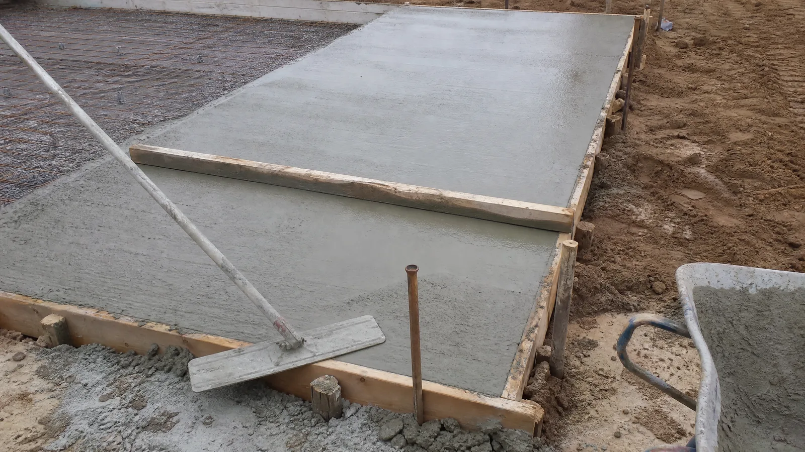 Freshly poured concrete slab between timber forms with a screed board resting across it