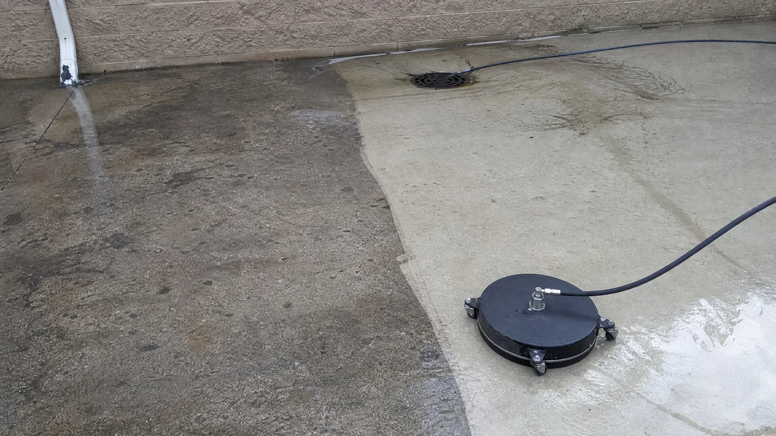 Concrete apron half cleaned by pressure washing, showing the line between grimy and clean concrete