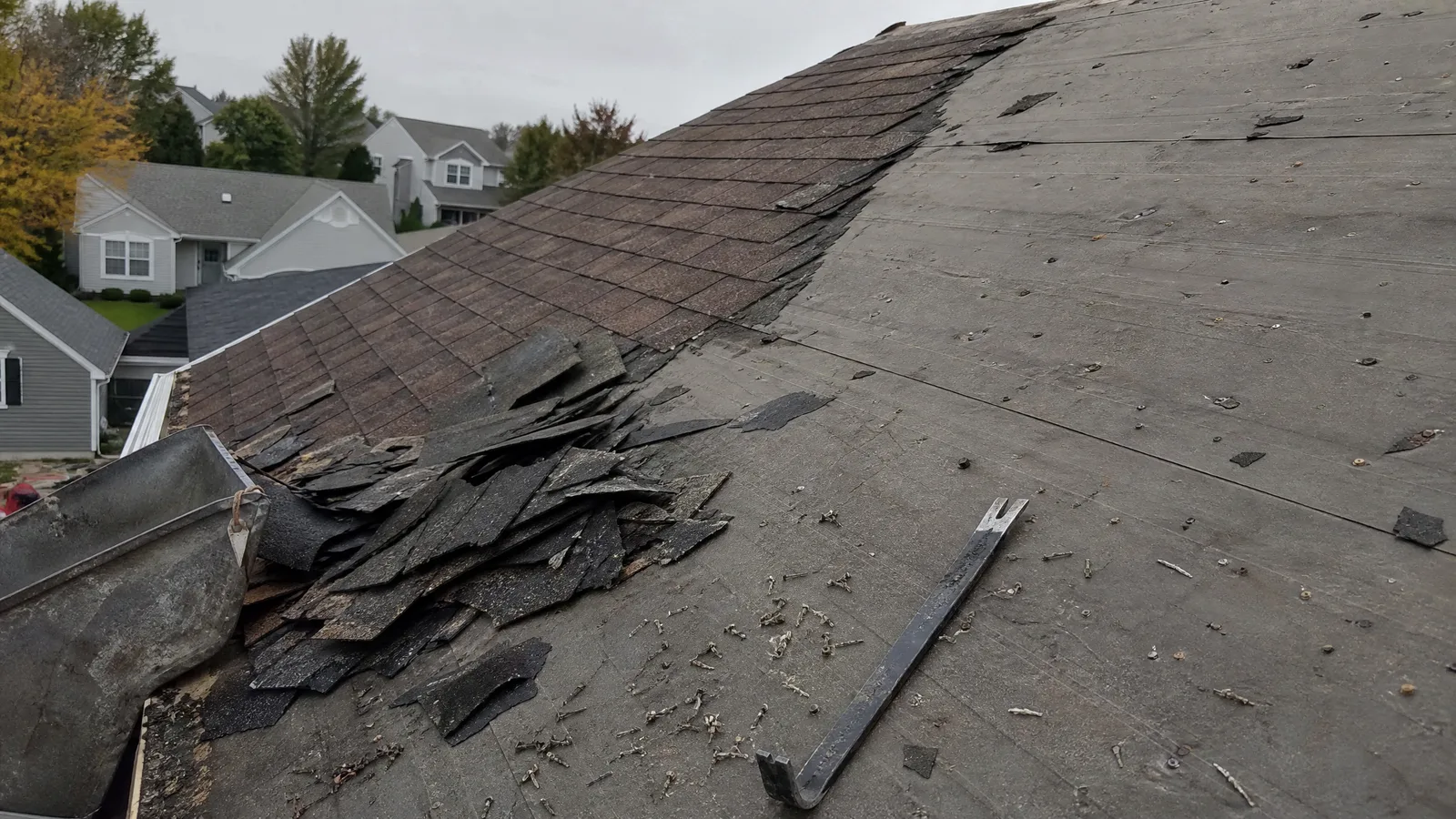 Partially stripped asphalt roof with torn-off shingles piled at the eave and underlayment exposed